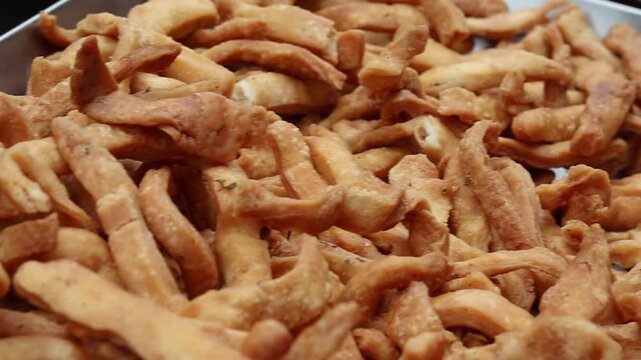 Close-up shot of a large pile of freshly fried, crispy golden-brown Namak Pare, a traditional savory Indian snack, displayed on a metal tray.
