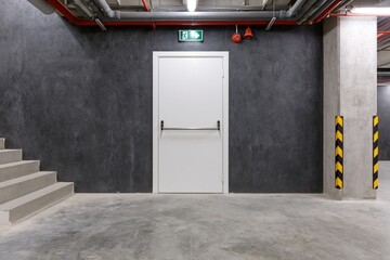 Obraz premium The White Industrial Door in a Concrete Basement Corridor with Staircase