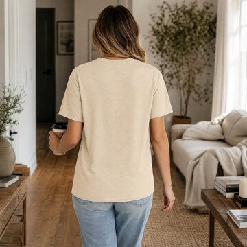 Woman wearing a beige t-shirt and blue jeans walks through a cozy living room while holding a disposable coffee cup.