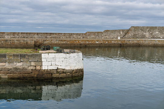 Lobster pots sit on the dock at a calm, cloudy Lossiemouth Harbour in Scotland