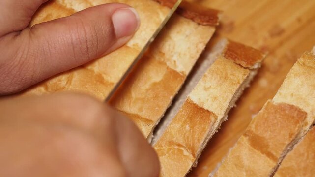 Close up of hand slicing fresh baguette bread on wooden cutting board slow motion