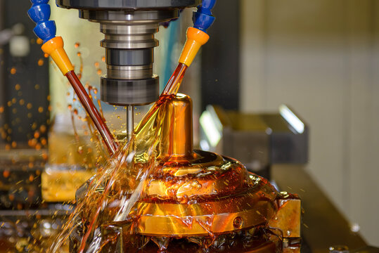 High-precision CNC milling machine performing a finishing cut on a brass shell mold part with a ball nose end mill tool using oil coolant.