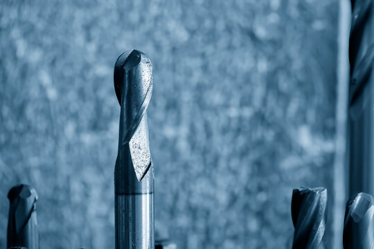 Macro close up scene of a ball nose end mill tool attached with particles of metal chips in a blue tone scene.