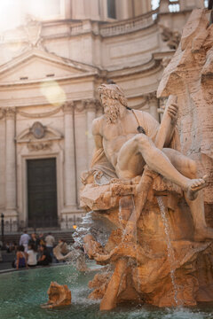 Sculpture of a river deity on Bernini's Fountain of Four Rivers, showing ancient art and architecture with a busy street scene in the background on a sunny day in the historic Italian capital