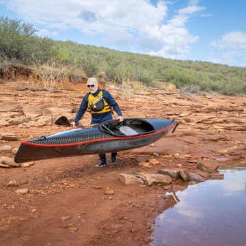 senior paddler is launching his decked touring canoe on shore of Horsetooth Reservoir - early spring scenery of Colorado foothills
