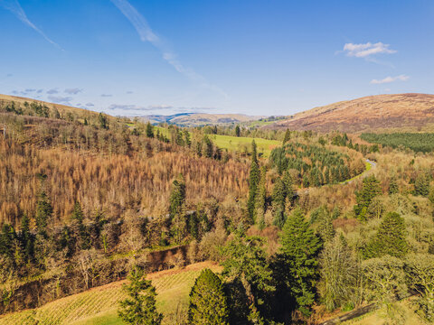 The River Esk winds through green fields and dense trees near Langholm in the Scottish Borders. This scene shows a clear view of the landscape near Langholm on the A7
