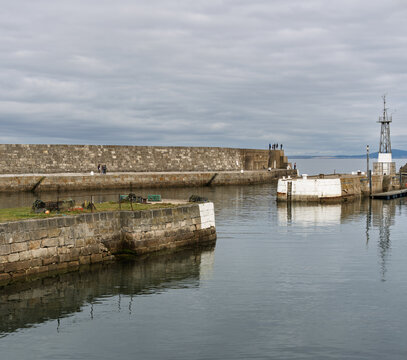 Stone walls bordering the water at Lossiemouth Harbour in Moray Scotland during a quiet and cloudy afternoon as visitors walk along the edge