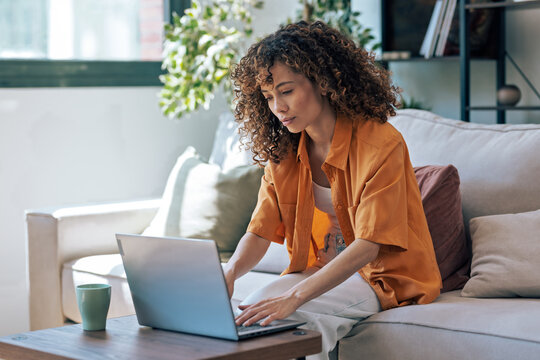 Concentrated woman working with her laptop while sitting on a couch at home