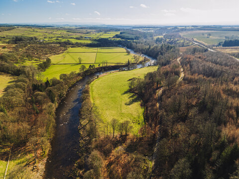 The River Esk winds through green fields and dense trees near Langholm in the Scottish Borders. This scene shows a clear view of the landscape near Langholm on the A7