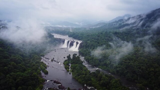 Aerial drone view of Athirappilly Waterfalls surrounded by lush rainforest and monsoon clouds in Kerala, India, showcasing the spectacular beauty of the Western Ghats.