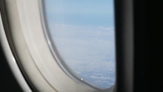 view through airplane window above the clouds and sky inspiration concept in cinematic aerial flying over white fluffy cloudscape in high altitude sky with fresh clean air and blue skies