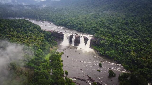 Aerial drone view of Athirappilly Waterfalls surrounded by lush rainforest and monsoon clouds in Kerala, India, showcasing the spectacular beauty of the Western Ghats.
