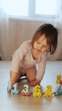 Vertical video. Toddler pulls a colorful number train across the floor during indoor play at home.