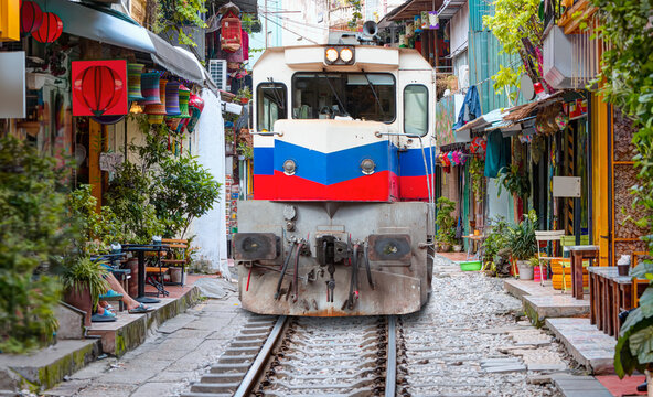 Red and Blue diesel train passing through the street - Hanoi city railway Perspective view running along narrow street with houses in Vietnam