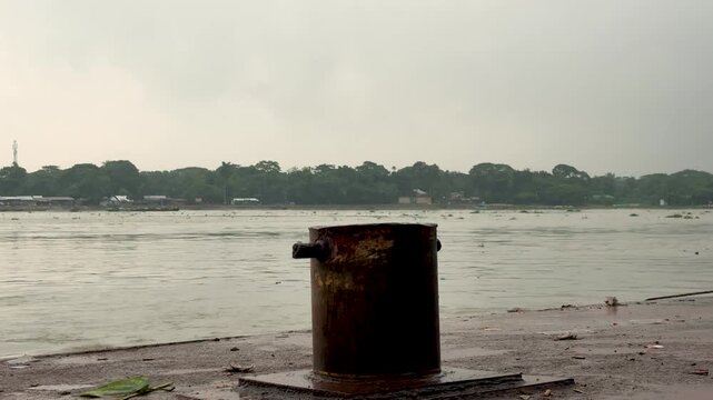 Rustic bollard by a tranquil riverbank under a cloudy sky with distant greenery