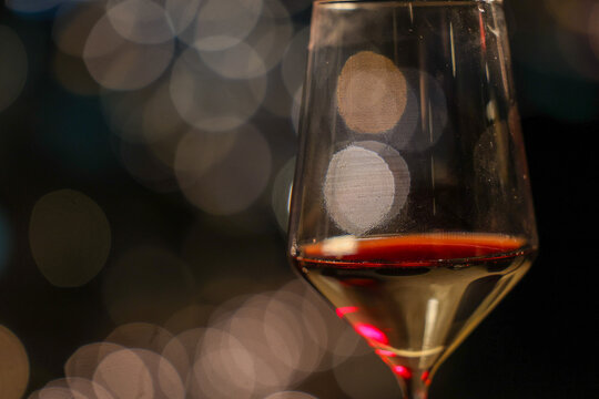 A close‑up of a wine glass with red wine against a softly blurred bokeh background, creating an elegant and atmospheric composition perfect for fine dining or celebration themes.