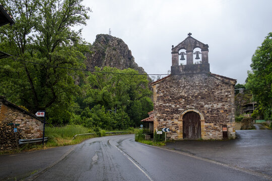 An ancient stone church with a traditional bell gable situated on a winding mountain road section along the Camino Primitivo route in Asturias, Spain