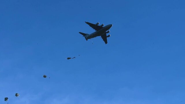 Military Transport Aircraft Performing Tactical Paratrooper Airdrop During Airborne Training Exercise Against Clear Blue Sky.