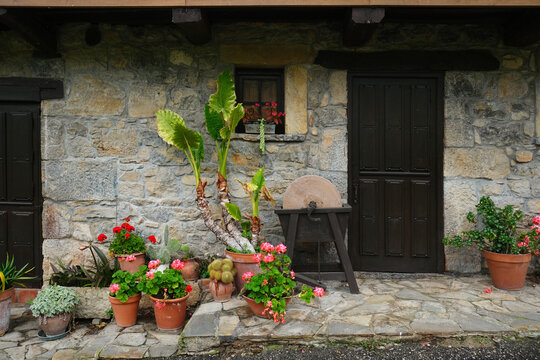 Rustic stone house facade with traditional dark wooden door and beautiful potted flowers in a Spanish village.