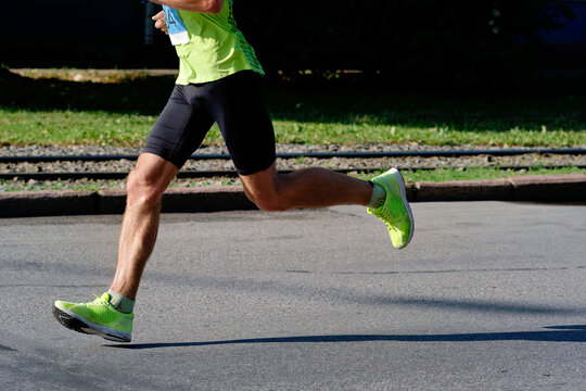 Side profile cropped shot of a male runner in neon sportswear sprinting on an asphalt road during a street marathon event