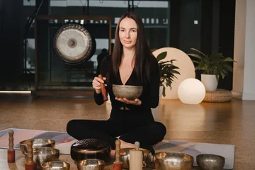 Fotobehang Lotusbloem A woman in the lotus position using a singing bowl indoors . Relaxation and meditation. Sound therapy, alternative medicine. Buddhist healing practices  © Alex
