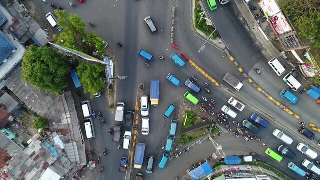 Aerial drone view of a busy traffic intersection with heavy congestion, cars, pickup trucks, and motorcycles navigating a crowded urban street junction surrounded by rooftops and buildings indonesia