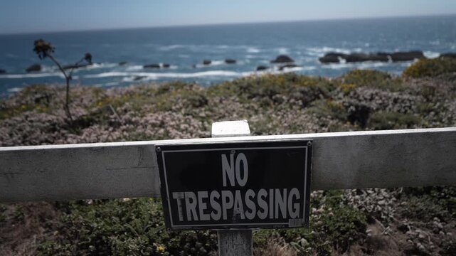 A no trespassing sign warns people to stay off the vegetation near Point Arena Lighthouse in Mendocino California by the ocean.