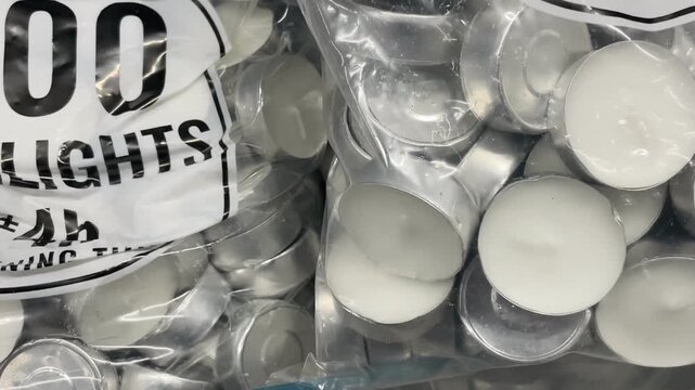 Closeup plastic bag containing a pack of 100 tea light candles displayed on a store counter. Close-up of packaged candles are arranged as retail merchandise in a shop.