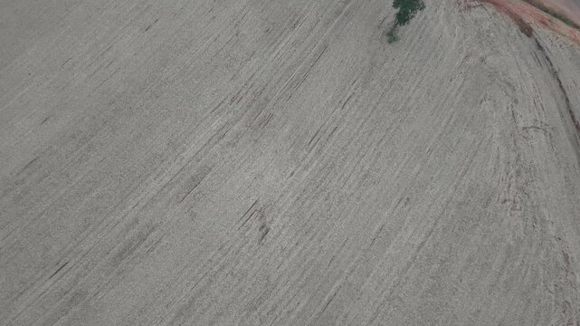 Aerial view of a dry agricultural field with tire tracks and a small green patch of vegetation