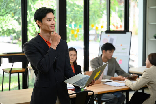 Confident Asian Business Leader Thinking with Laptop During Team Meeting in Modern Office