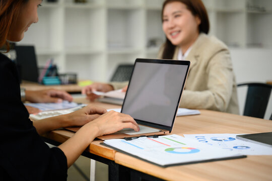 Close up of Two Asian Businesswomen Collaborating in Modern Office with Laptop and Financial Charts