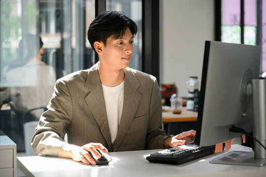 Young Asian Businessman Working at Desktop Computer in Modern Office Workspace