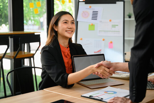 Smiling Asian Businesswoman Shaking Hands with Colleague in Modern Office Meeting Room