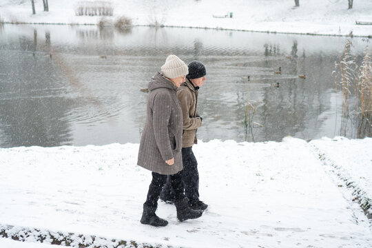 Senior couple walking arm in arm on snowy path. Love knows no age for a loving couple. Tenderness survives cold and affection warms more than clothing. Devoted partners embracing in winter landscape