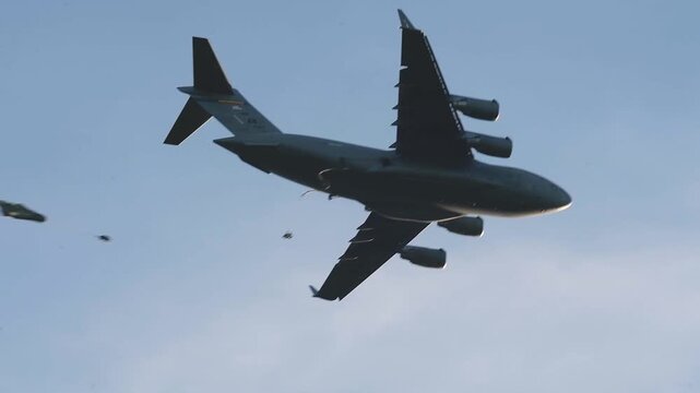 Military Cargo Aircraft Conducting Paratrooper Airdrop During Tactical Airborne Training Mission Beneath Clear Blue Sky Successfully.