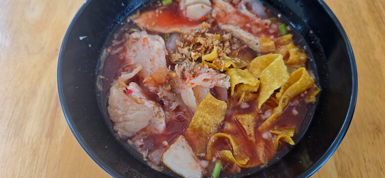 Yentafo served in black cup. pink noodles. This pink noodle soup comes with various toppings such as fish balls, crispy squid, jellyfish, and crispy fried dumplings. Pickled bean curd is also included