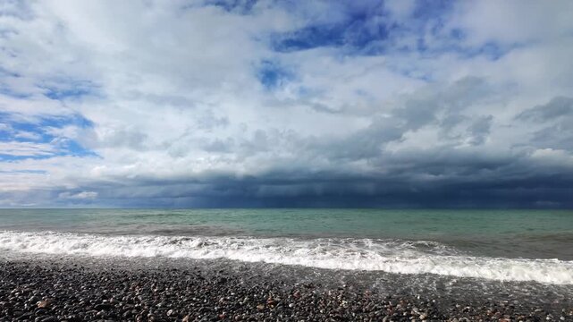 Foamy waves crash onto a dark pebble beach beneath a stormy sky in batumi.
