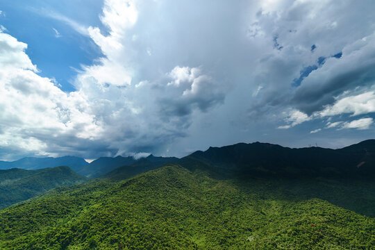 Massive gray clouds hover over the vibrant tropical slopes of the mountains in Hong Kong as daylight shifts across the landscape during the middle of the day