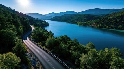 Fototapeta premium Serene winding road alongside a sparkling blue lake in a mountainous landscape
