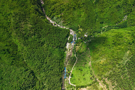 Green mountain slopes surround a small winding river with several tents pitched along the bank in the middle of a lush tropical wilderness area during the day