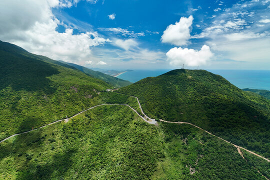 Lush green mountains slope down toward the blue ocean waters under bright summer skies with a winding road cutting through the landscape at Hai Van Pass
