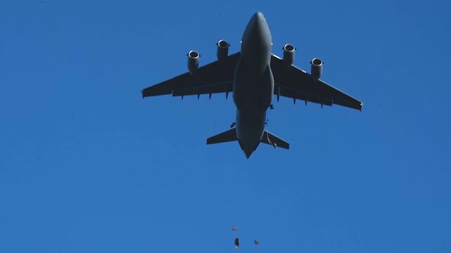Military Cargo Aircraft Conducting Precision Paratrooper Airdrop During Airborne Training Mission Beneath Clear Blue Sky.