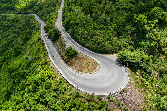 Curvy asphalt road winds through steep green forested mountainside on the famous Hai Van Pass in Vietnam under bright daylight as people travel the steep route