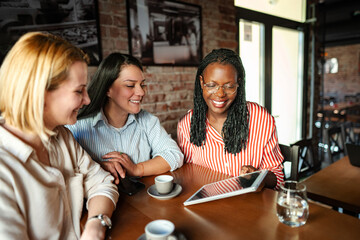 Fototapeta premium Diverse women friends smiling using digital tablet in cafe