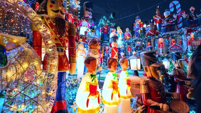 Nutcracker and choir figures at Dyker Heights Christmas display. Snowy night yard contains illuminated toy soldiers, singers, snowmen and cartoon figures among dense holiday lights.