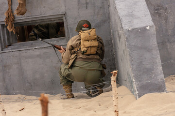 Fototapeta premium Historical reenactment. A World War II-era American infantry soldier fights on a beach near a bunker