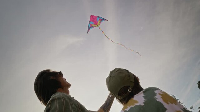 Caucasian father and young son flying colorful kite against sky, looking up together. Footage serves well for family bonding, outdoor recreation, and parenting marketing campaigns