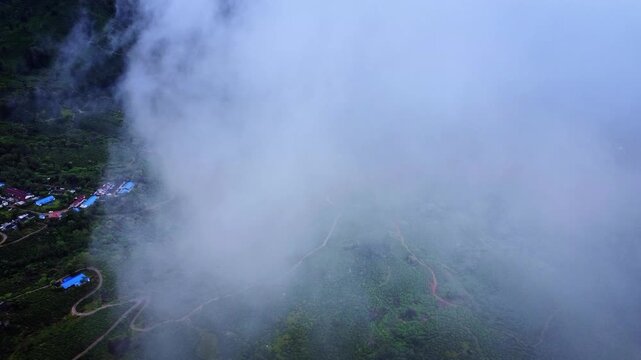 Aerial drone view of the misty landscape of Munnar during the monsoon season, featuring lush green hills, a winding river, and low clouds in the Western Ghats of Kerala, India.