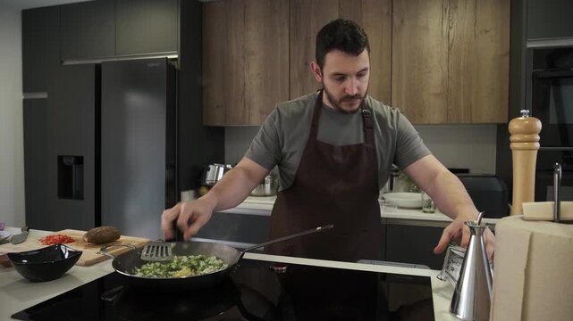 Male chef with an apron seasoning and sauteing vegetables in a frying pan on an induction cooktop