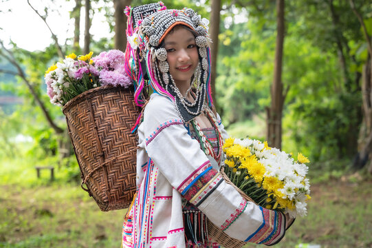 Young Akha hill tribe girl in vibrant handcrafted traditional costume holding fresh flowers in a lush green forest, Northern Thailand